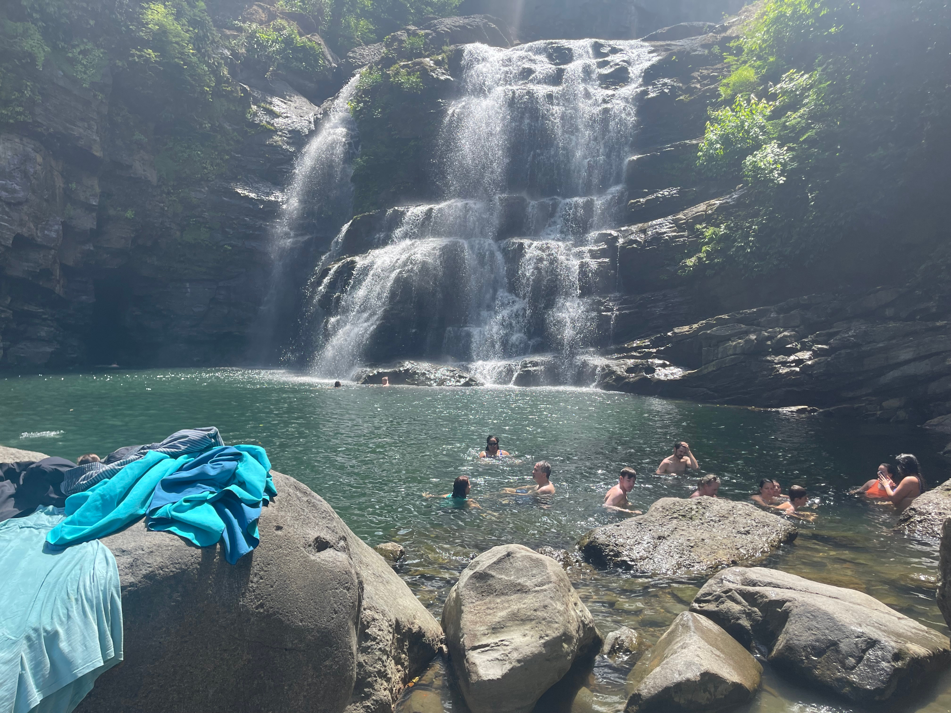 Family swimming in the pool at the base of Nauyaca Waterfalls with water cascading down rocky tiers