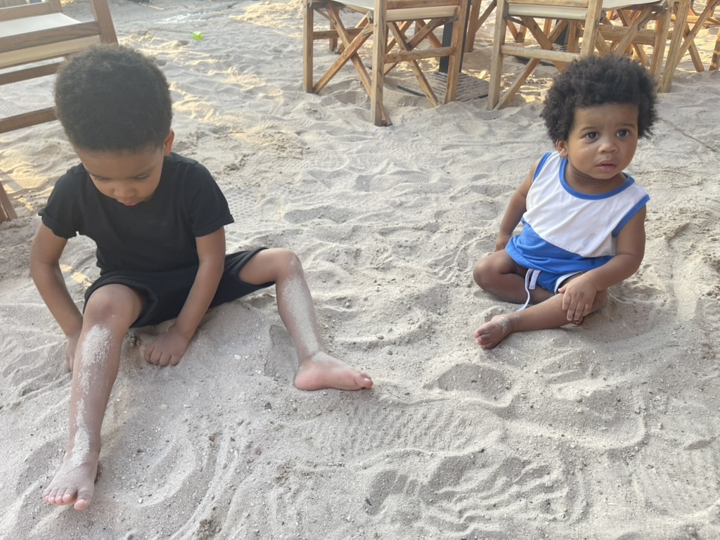 Two young brothers sitting and playing in the sand beside beachfront tables