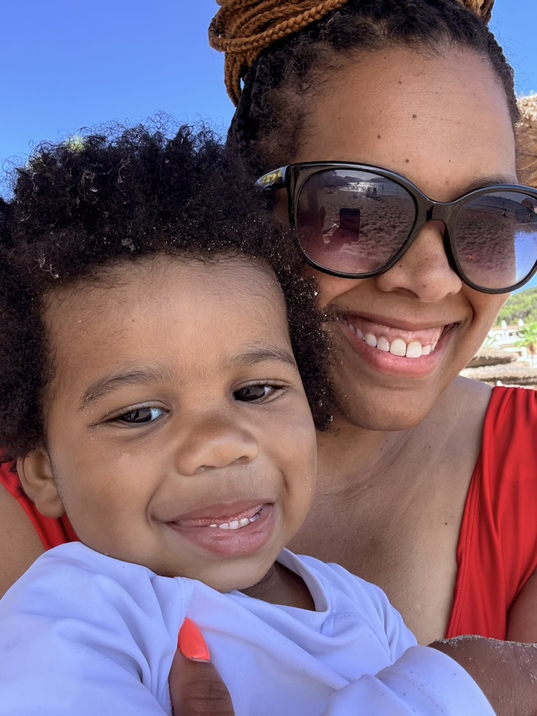 Mom and toddler smiling close together on the sand at Sant Elm