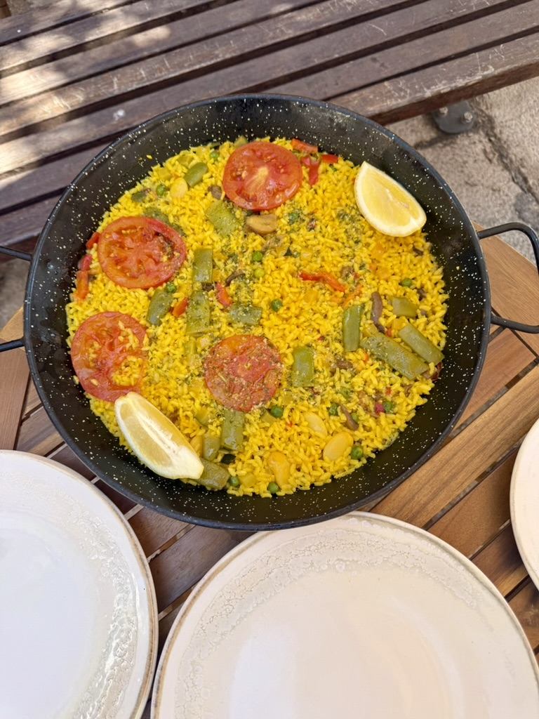 A pan of vegetable paella with tomato slices and lemon wedges on an outdoor table at Alchemy