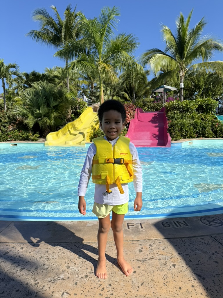 Preston in a yellow life vest in front of the small slides and shallow pool at Turtle Beach