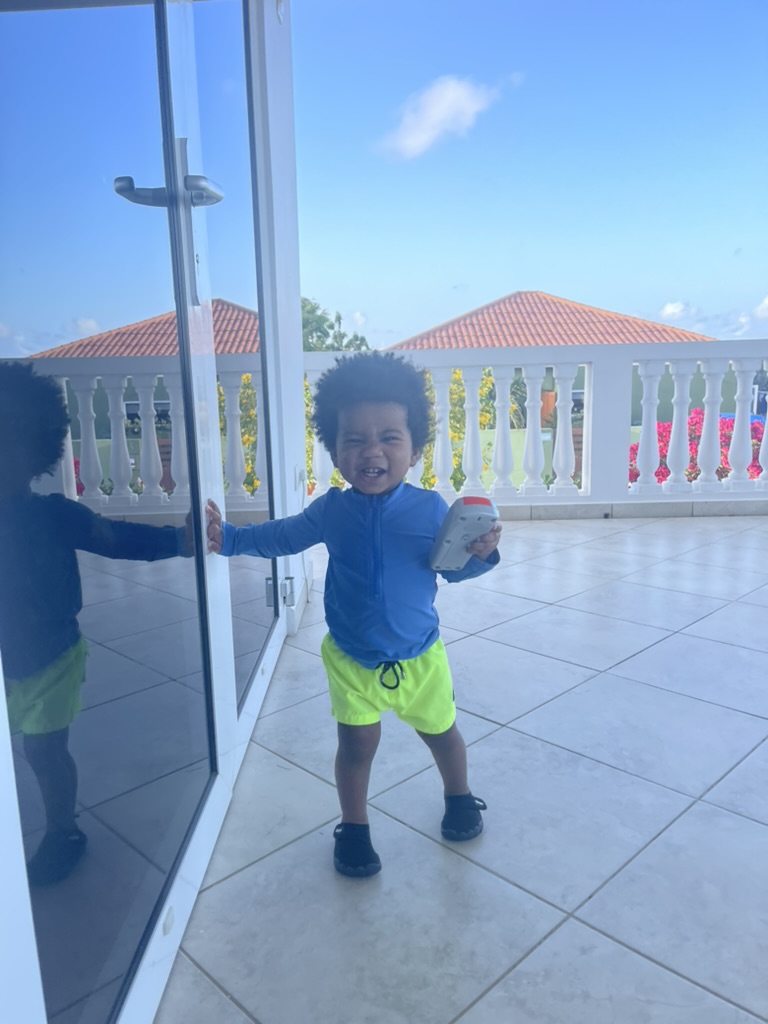 Toddler laughing on the villa balcony with red-tiled rooftops behind him