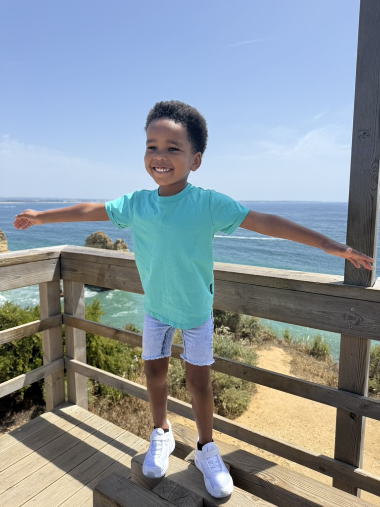 Boy with arms outstretched on the wooden boardwalk above the ocean at Ponta da Piedade