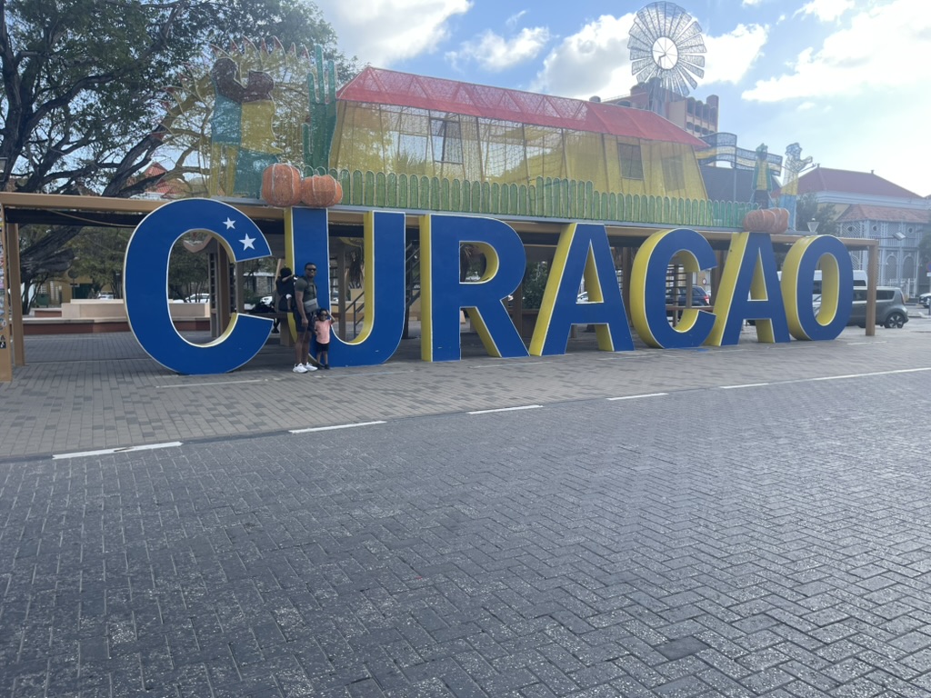 Large blue and yellow CURAÇAO letter sign with a father and child standing beneath it
