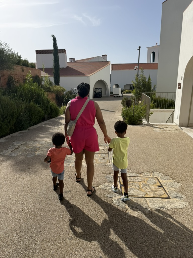 Mom walking hand in hand with the boys along a path between the white resort buildings