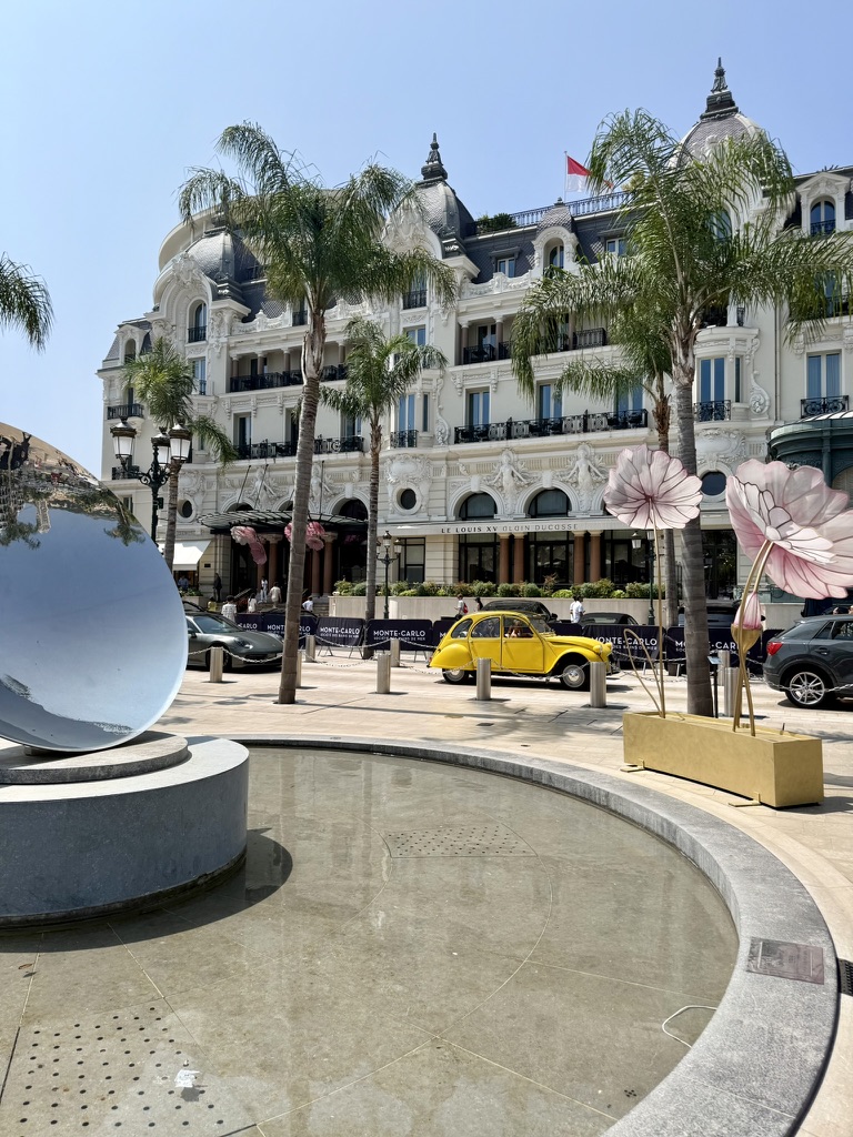 Casino Square in Monte-Carlo with palm trees, the Hôtel de Paris facade and a yellow vintage car parked out front