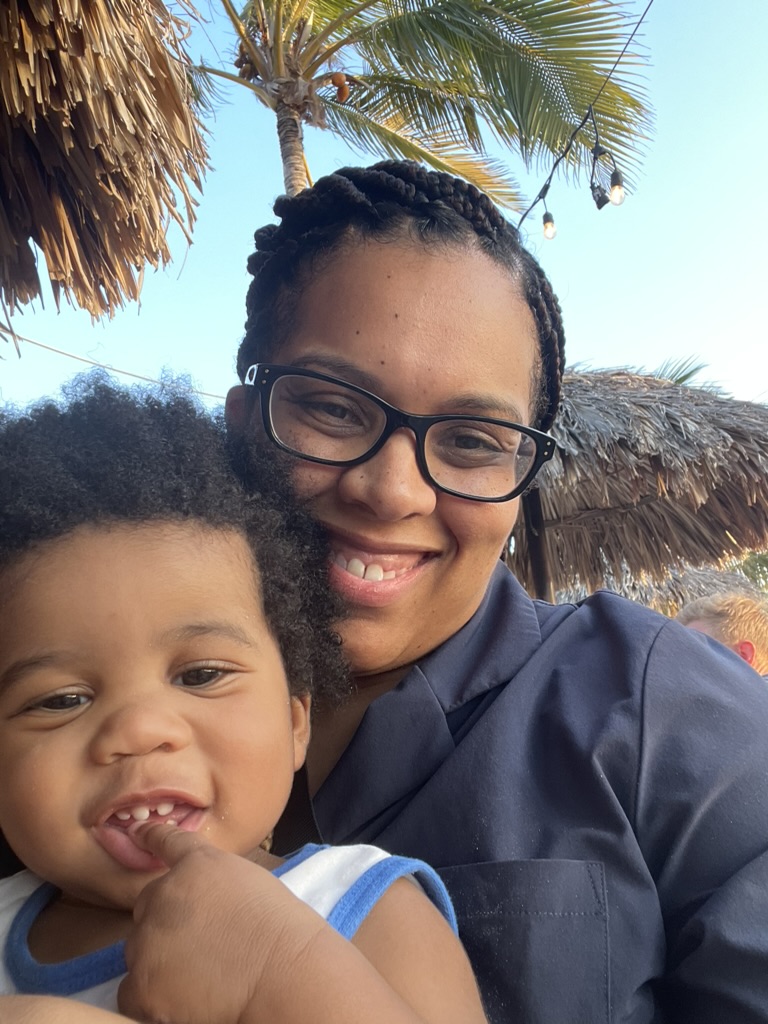 Mother holding her toddler under palm trees and string lights at the beach restaurant