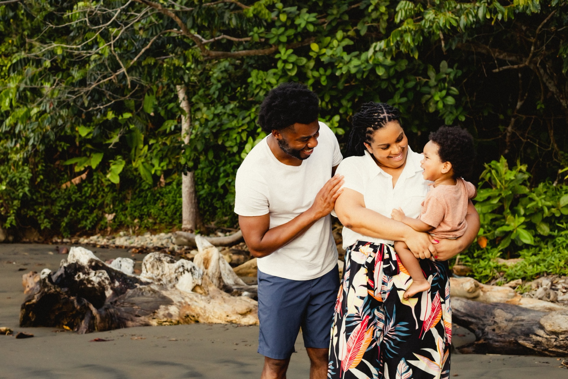 A family together on a sandy beach backed by dense green tropical foliage and driftwood