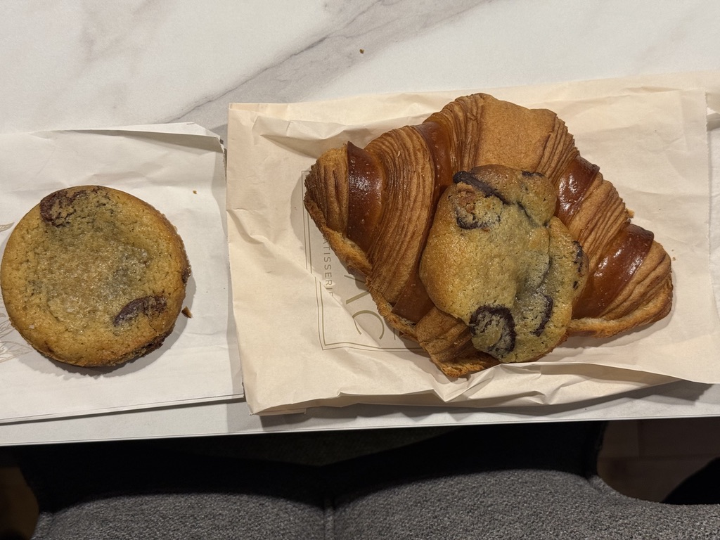 A chocolate-chip cookie croissant and a chocolate-chip cookie on pastry paper.