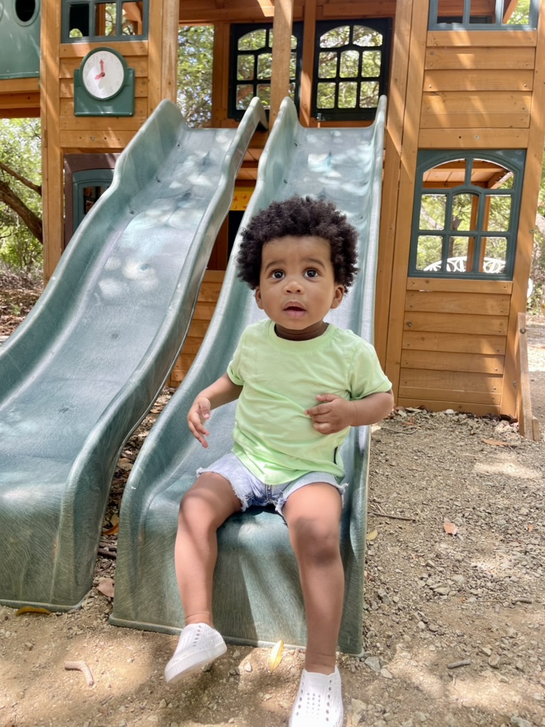 Toddler sitting at the bottom of a wooden playground slide