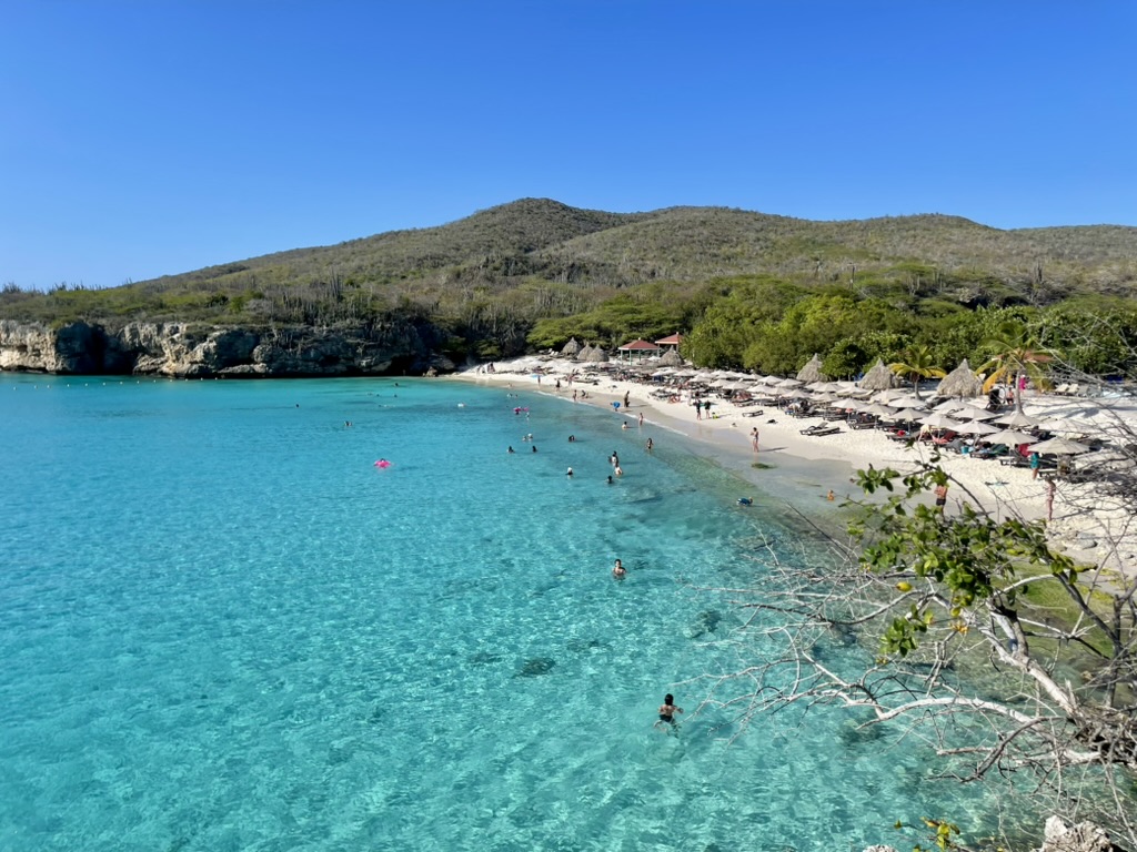 Wide view of Grote Knip's turquoise water, white sand and thatched umbrellas below a green hillside
