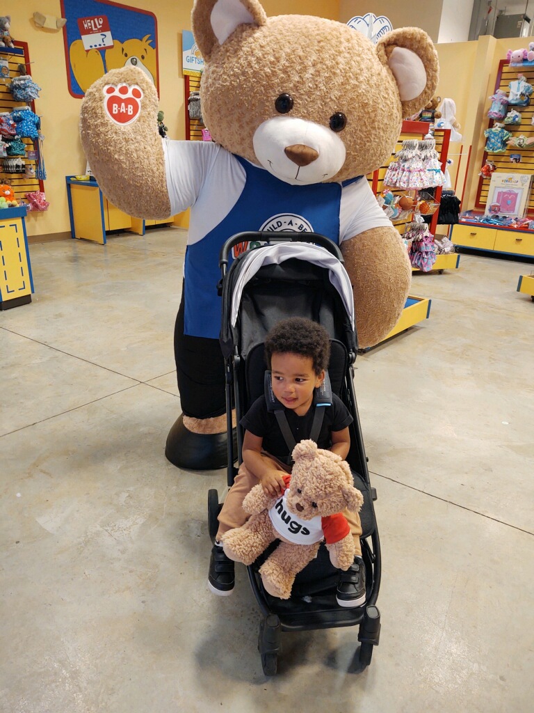 Toddler in a stroller holding a new Build-A-Bear teddy inside the store