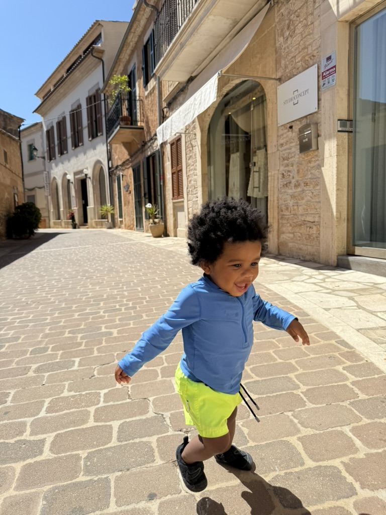 A toddler running down a quiet cobblestone street in Santanyi lined with sandstone buildings