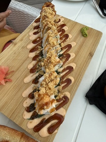 Long sushi roll topped with crunch and sauces on a wooden board