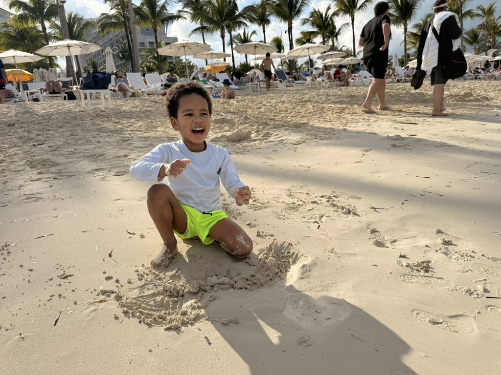 Preston laughing while digging in the sand on the busy main beach at Baha Mar