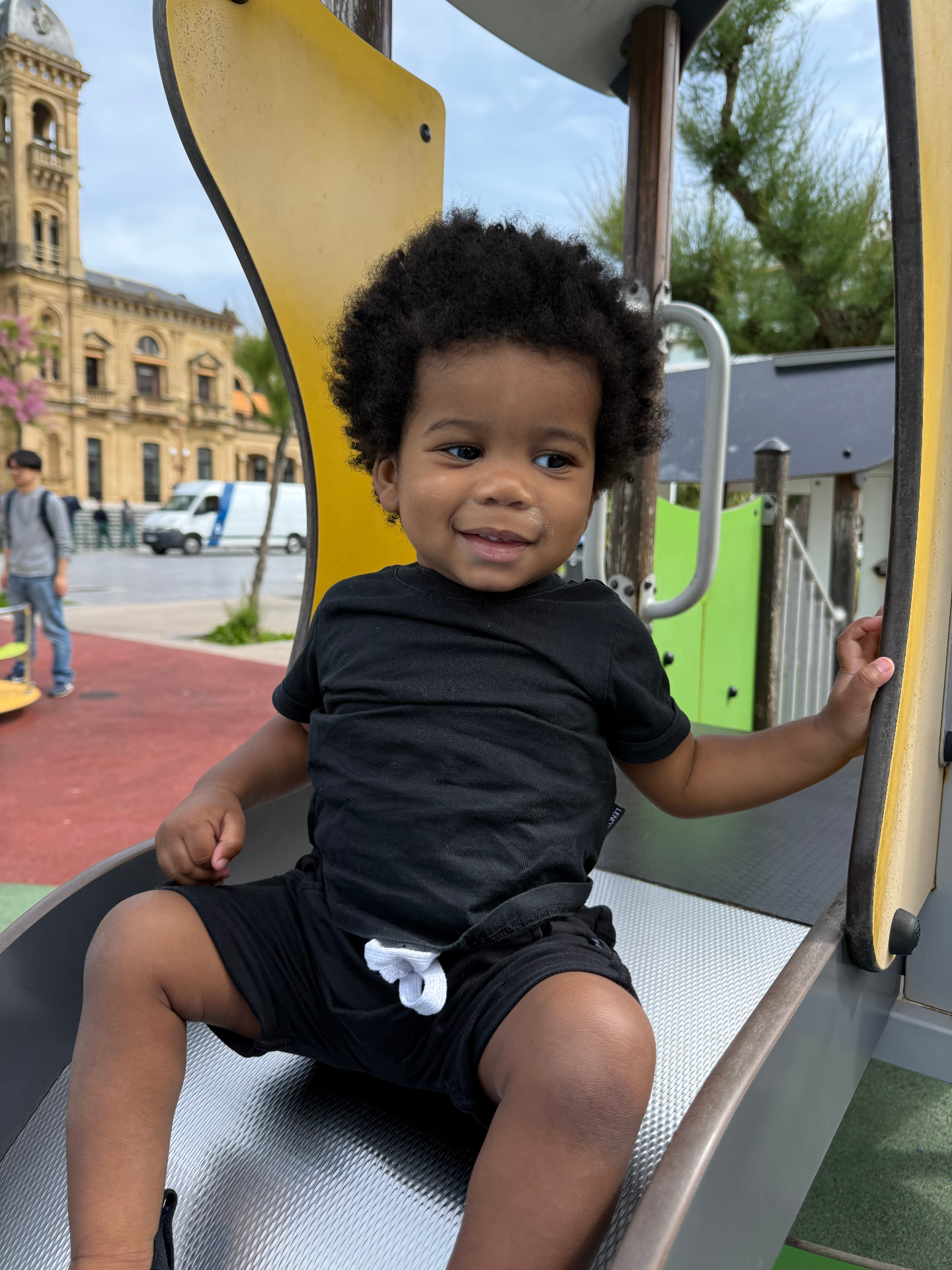 A young child sitting on playground equipment in a European city square