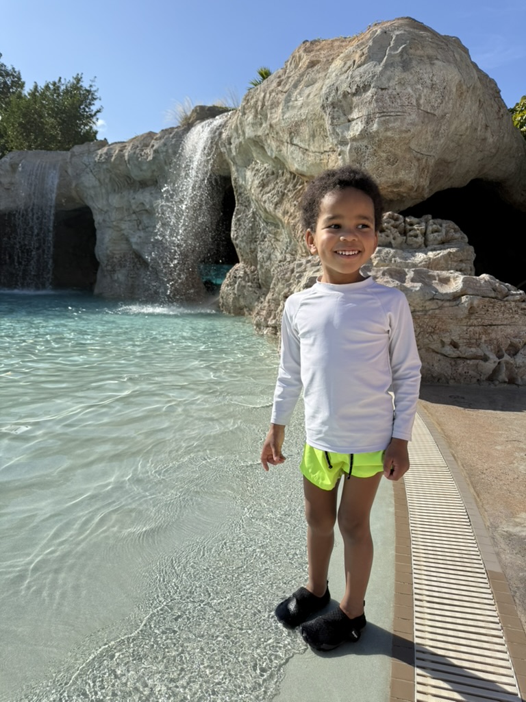 Preston standing at the zero-entry edge of Dean's Blue Hole in front of the waterfall and grotto