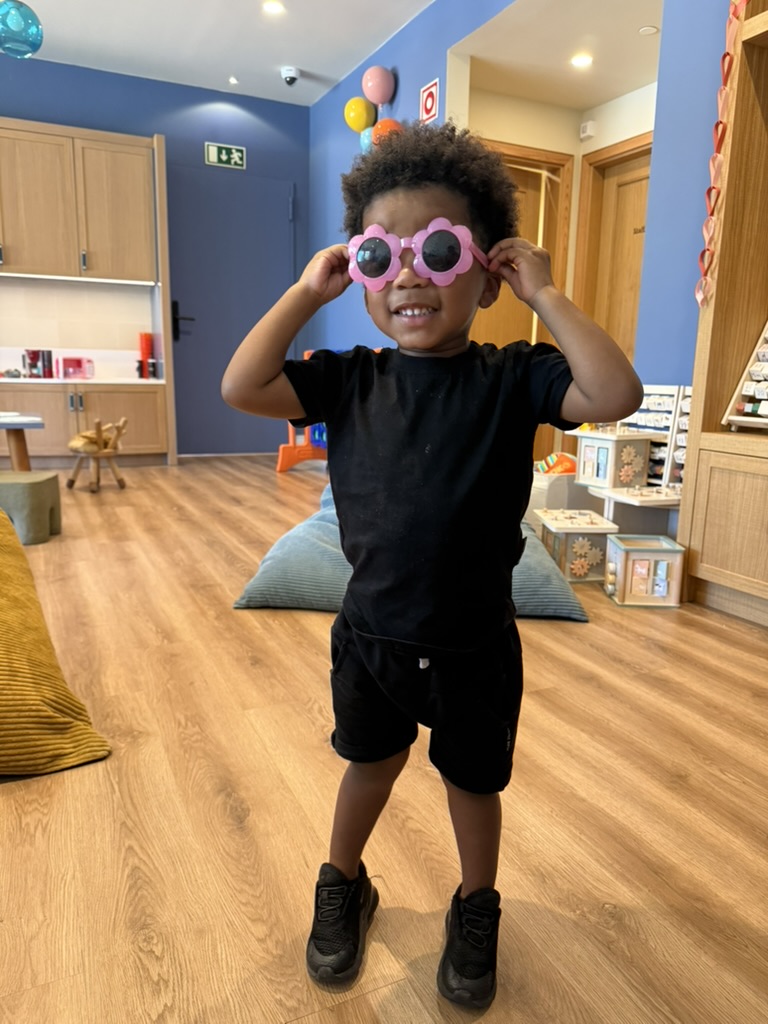 Smiling child holding up pink flower-shaped sunglasses in a bright playroom