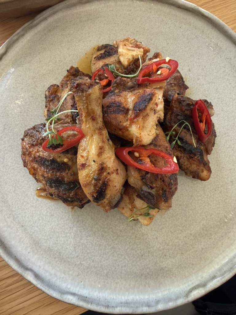 Plate of charred grilled chicken pieces topped with sliced red chilies and herbs
