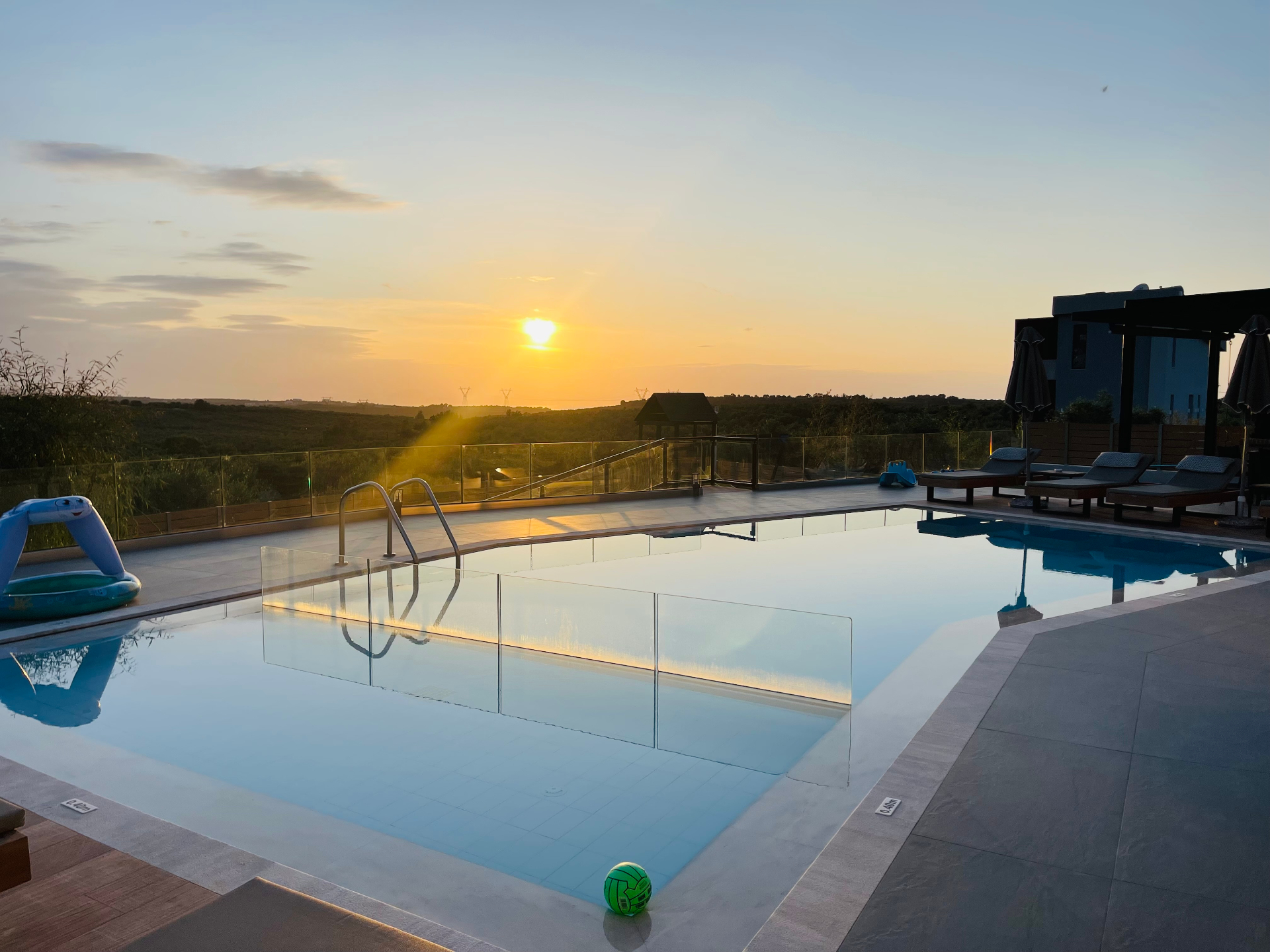 A rooftop infinity pool at sunset with a child's inflatable float and a small green ball