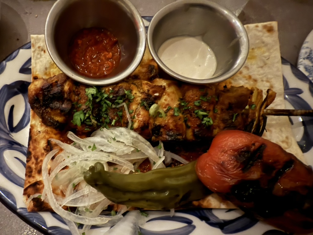 A grilled chicken skewer on flatbread with onions, blistered pepper and tomato at Cleo Mediterráneo