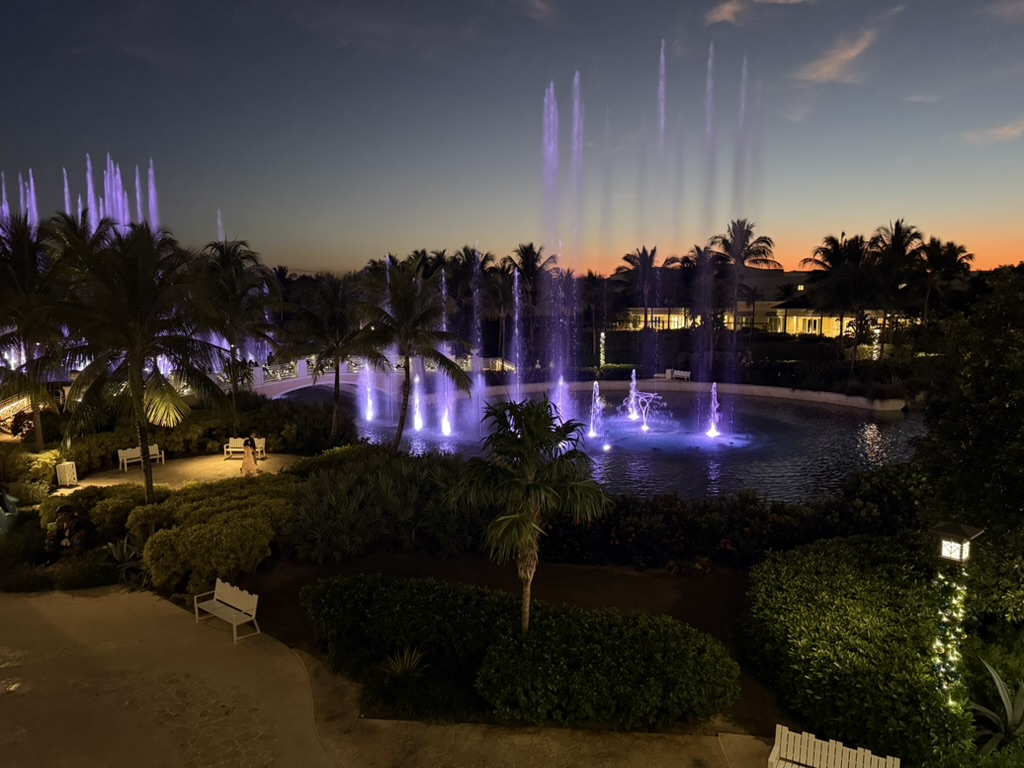 The Baha Mar fountain show lit purple at dusk with palms and the resort behind it