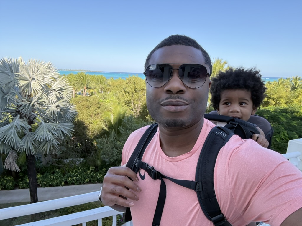 Dad on the balcony with Avery in a hiking carrier, palms and turquoise water behind them
