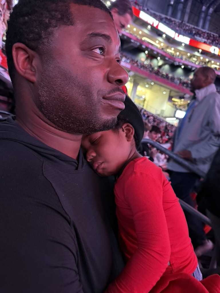 Father holding a sleeping toddler in a red shirt against his shoulder in the stadium seats after the Falcons game