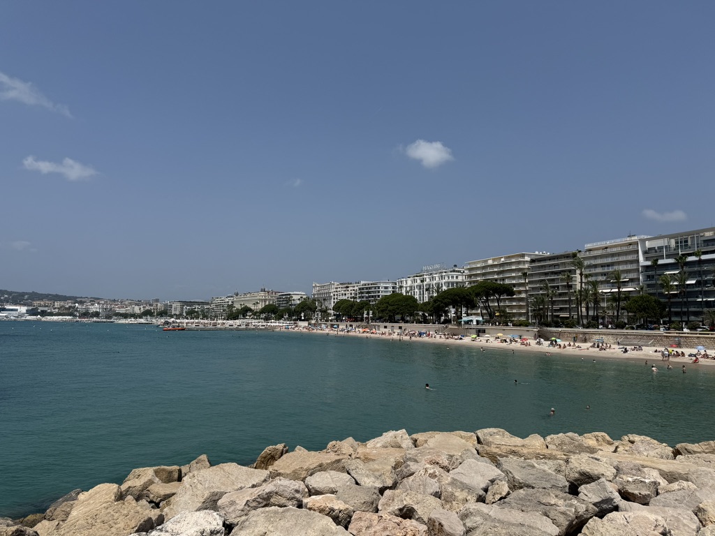 The Cannes waterfront with turquoise water, a rocky breakwater and the Croisette hotels along the beach.
