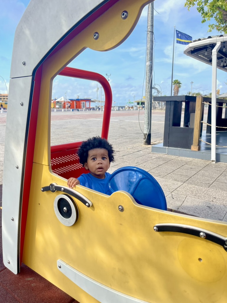 Toddler sitting in a boat-shaped playground structure on the waterfront