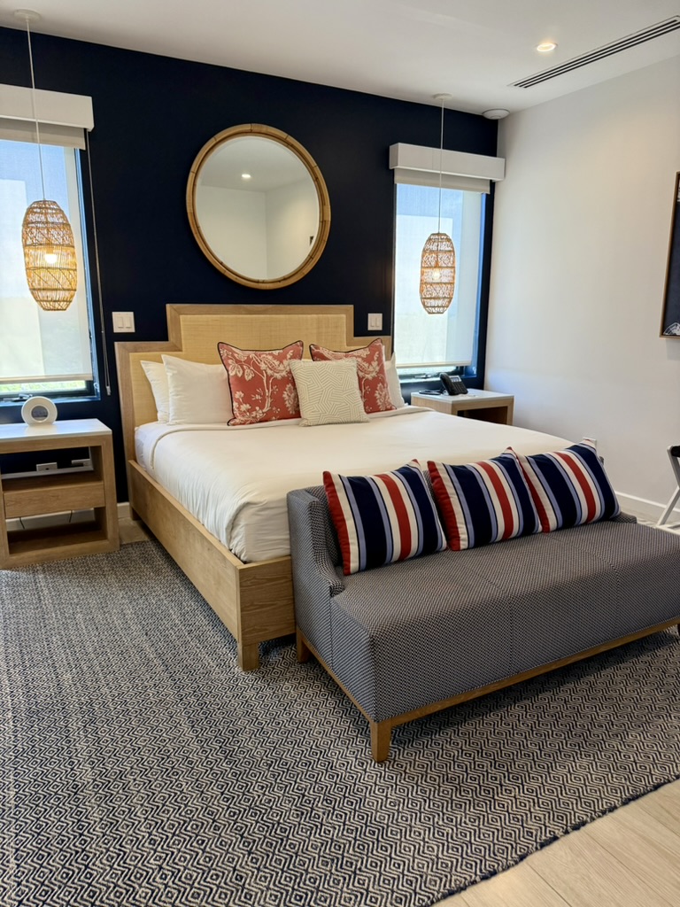 King bedroom with rattan mirror, navy accent wall and striped bench