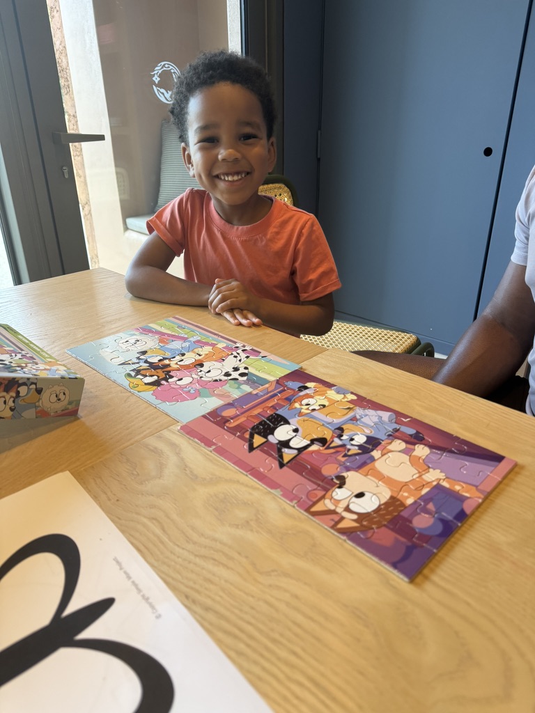 Smiling boy at a wooden table with two completed cartoon puzzles in front of him