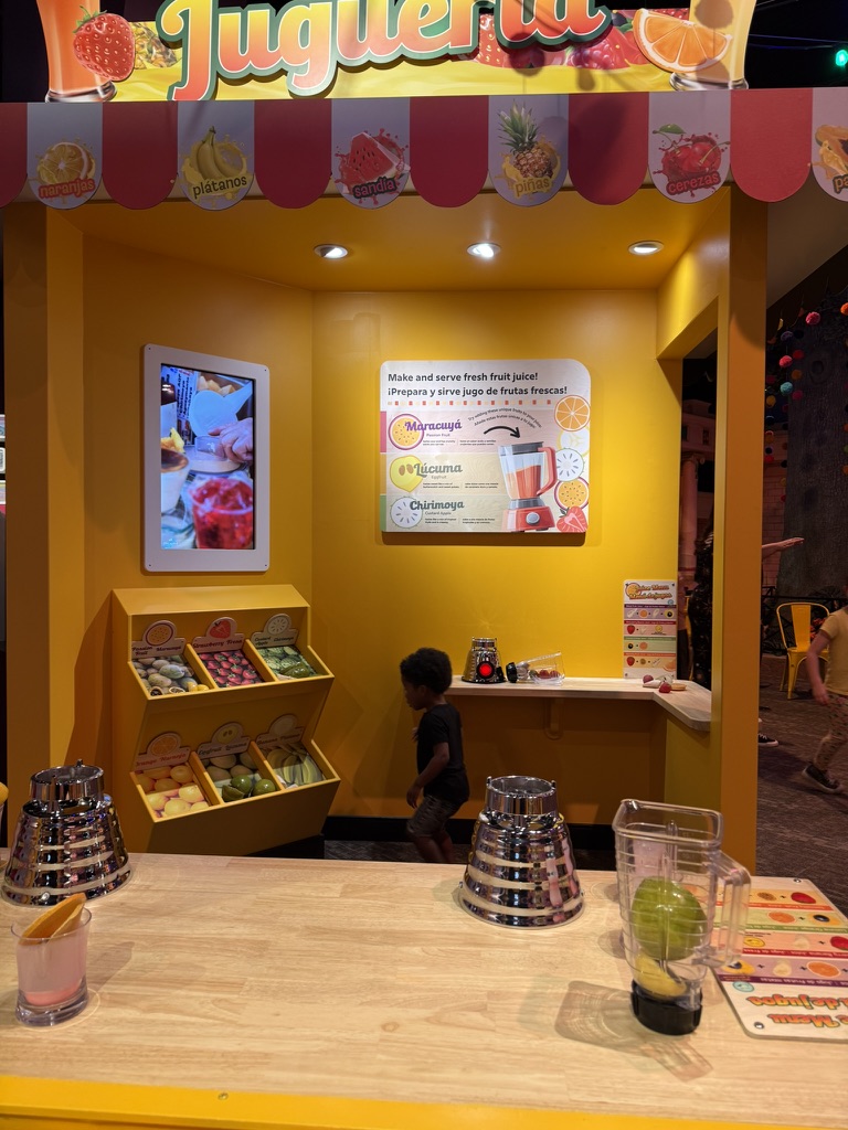 Avery exploring the bright yellow jugueria juice stand in Take Me There: Peru