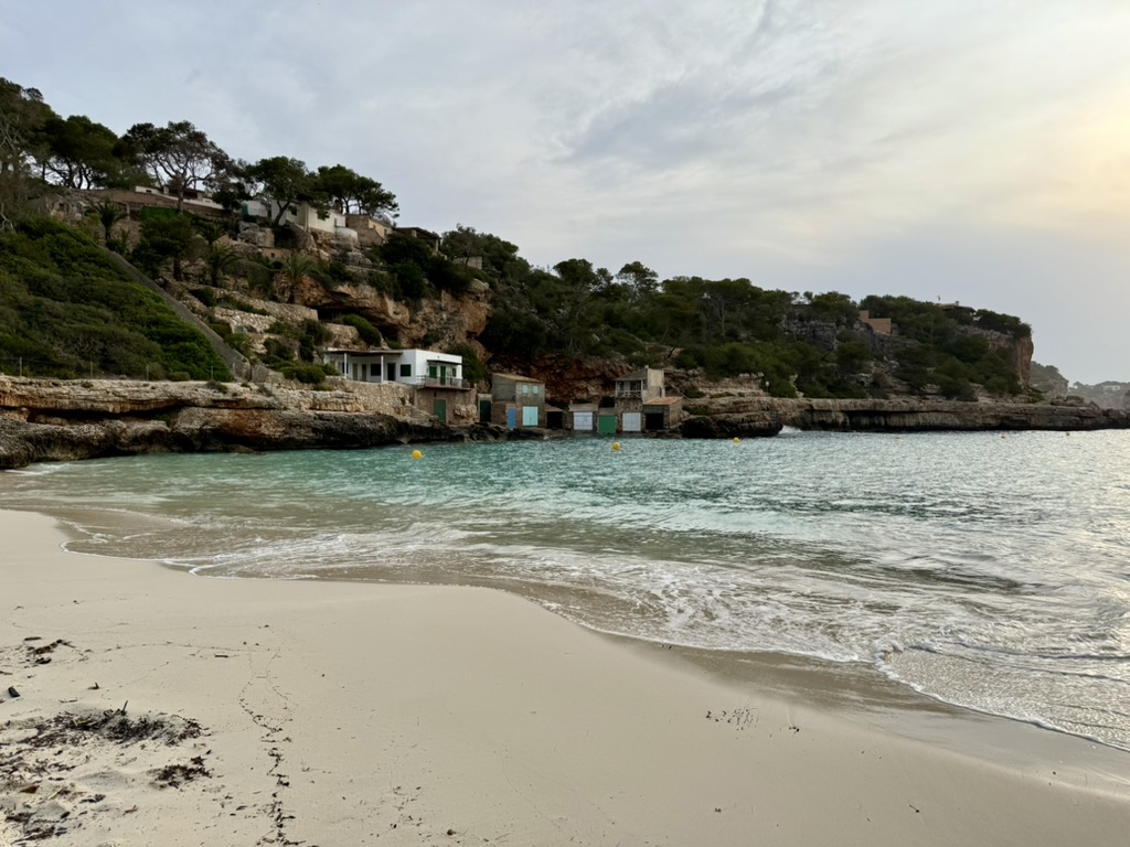 Cala Llombards at sunrise with empty sand, turquoise water and cliffside boat houses