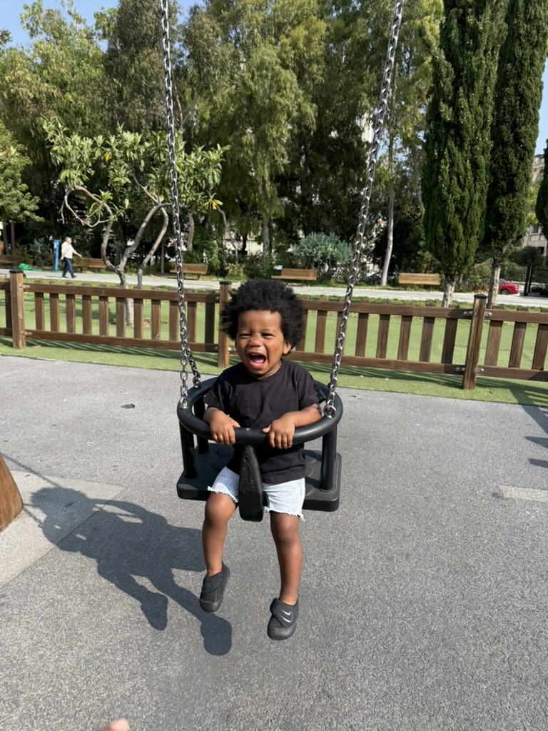A young child laughing on a bucket swing in a sunny Nice park