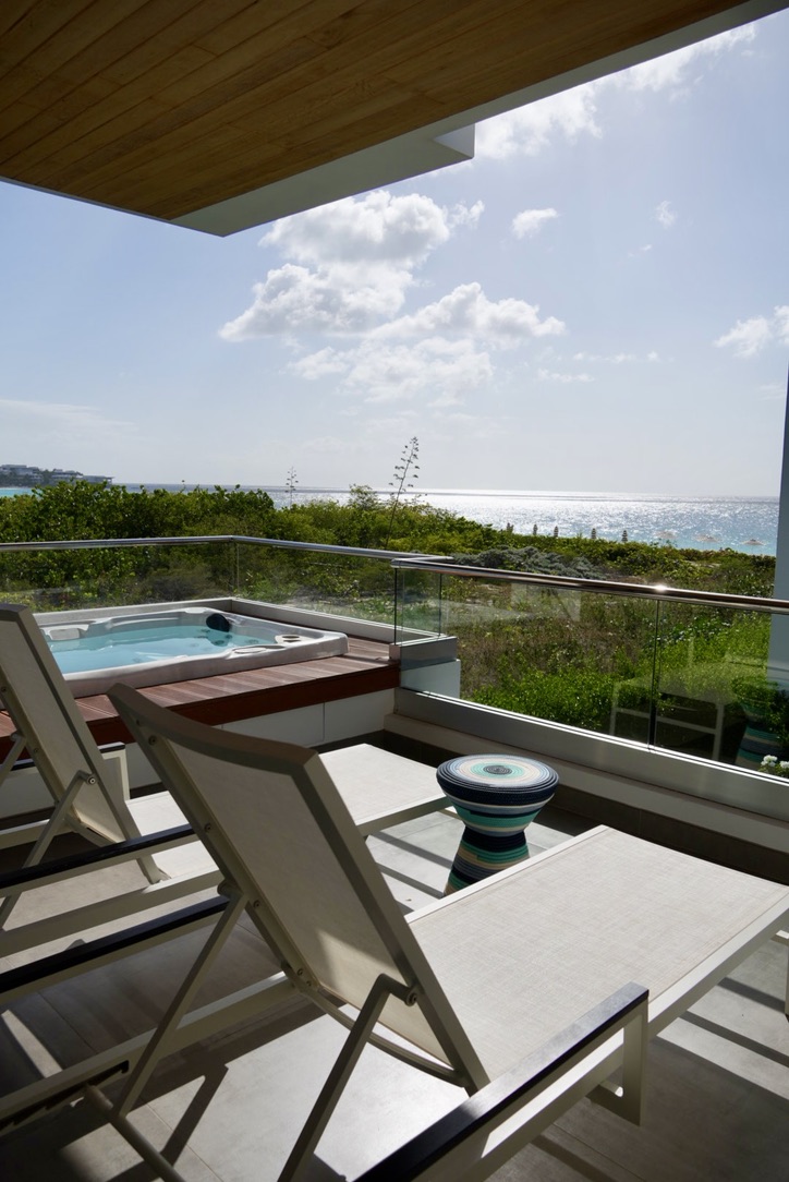 Villa balcony with a private hot tub, loungers and a partial ocean view over the greenery