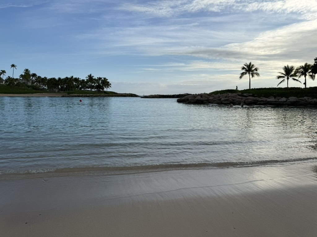 Calm Ko Olina lagoon at golden hour with palm trees along the rocky breakwater