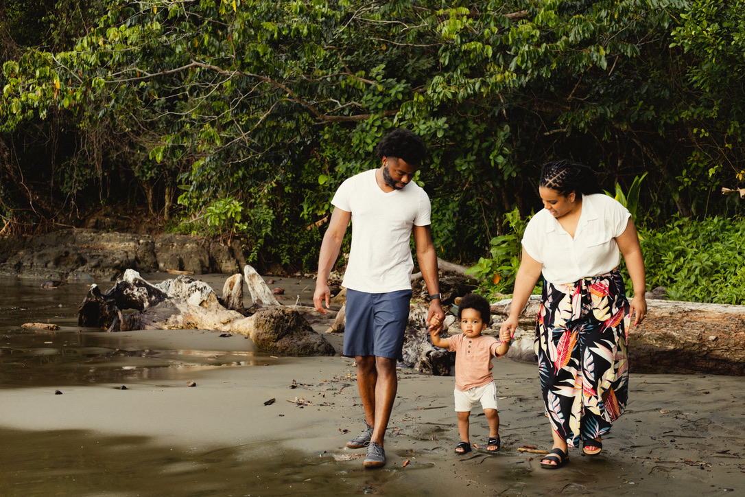 A family walking together on a sandy beach with lush green trees in the background in Costa Rica