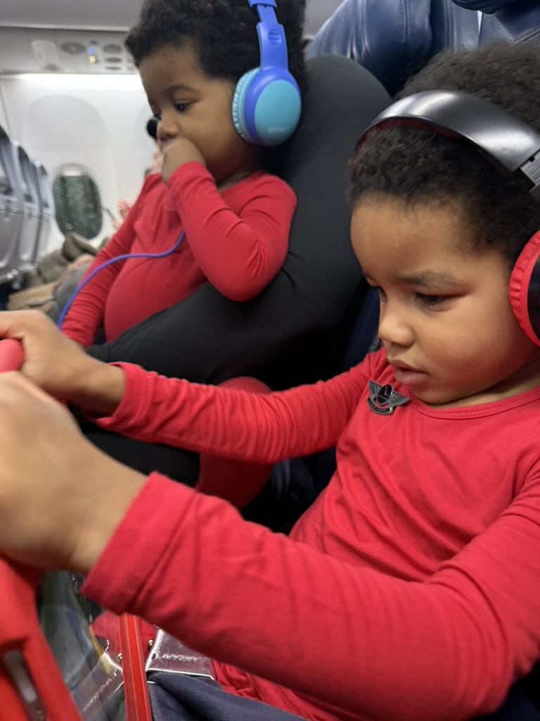 Both boys in matching red pajamas wearing headphones in their airplane seats