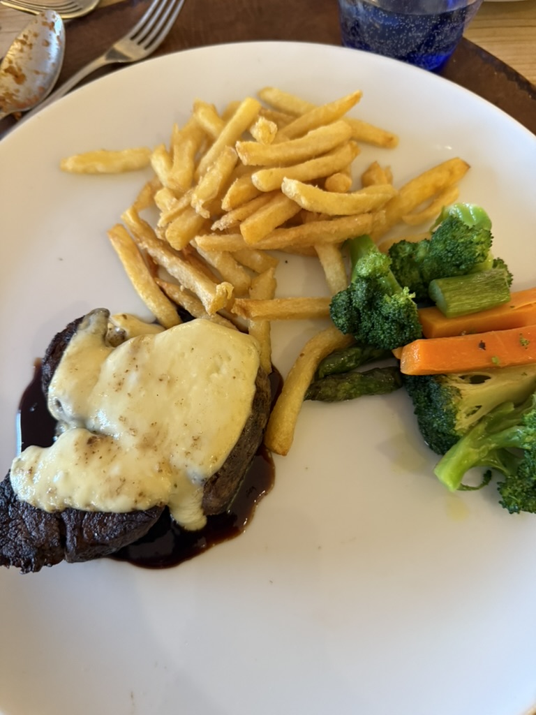 Plate of steak topped with melted cheese, fries and steamed vegetables at Cala Conills