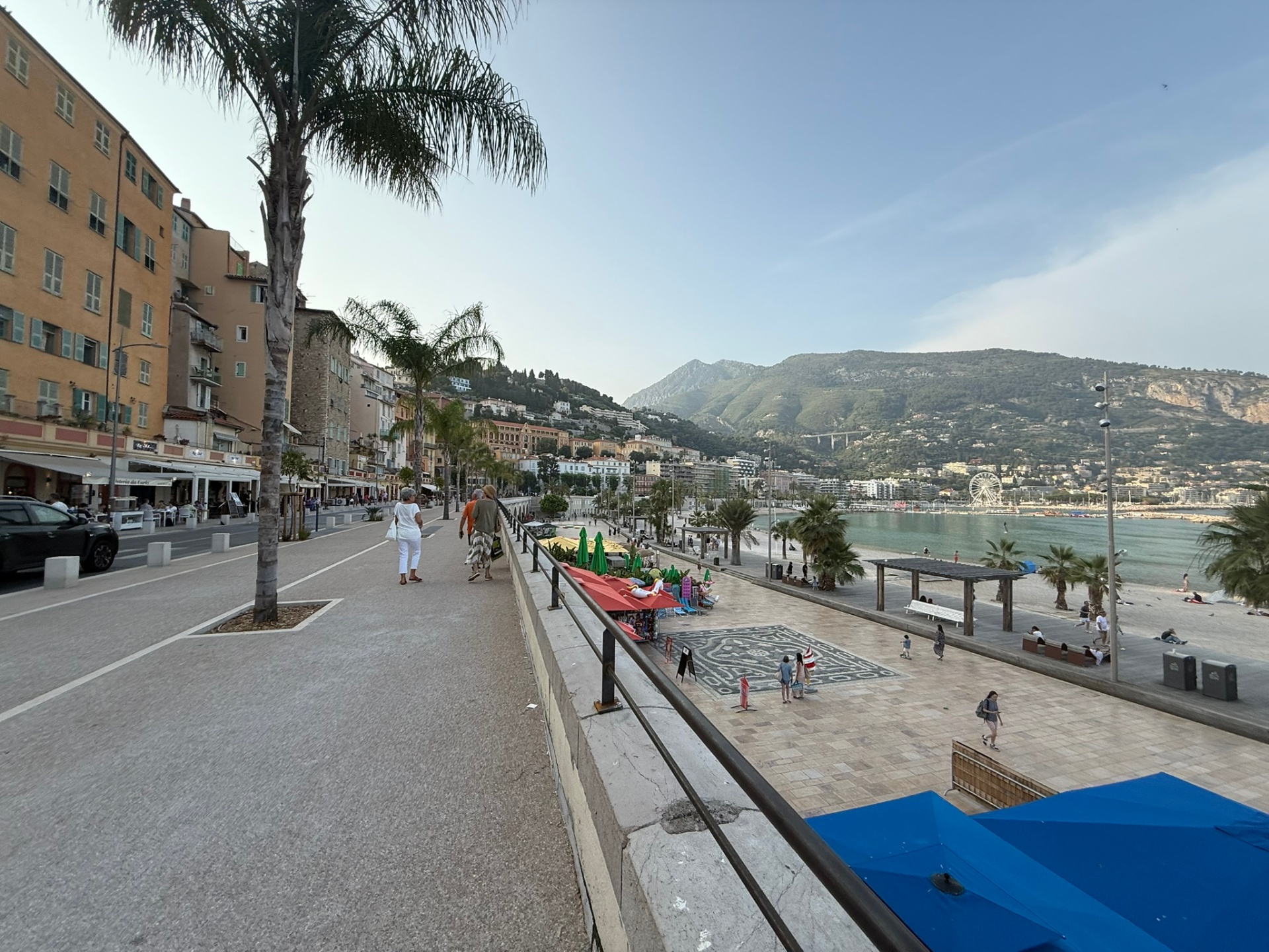 Palm-lined promenade in Menton looking down over the beach, ferris wheel and mountains beyond