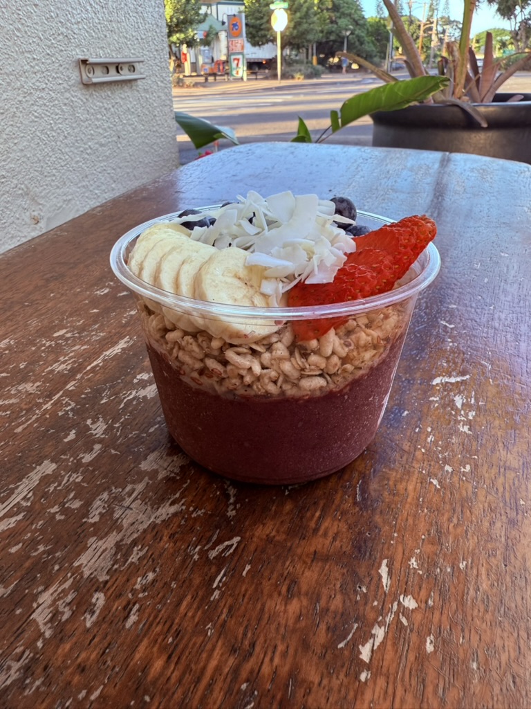 An açai bowl topped with banana, coconut, granola and strawberry on a weathered wooden table