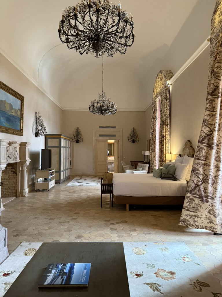 The Elegant Suite with vaulted ceilings, two chandeliers and a large bed beside tall curtained windows