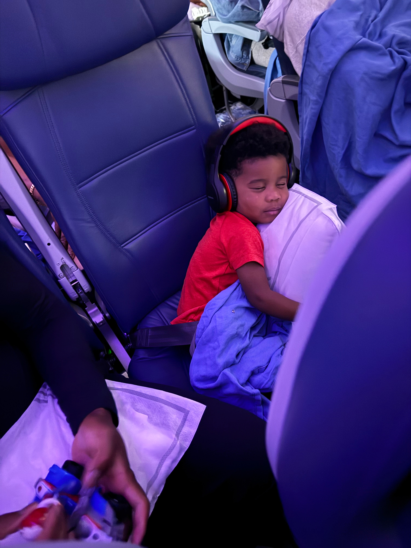 A child wearing headphones rests against a pillow in an airplane seat