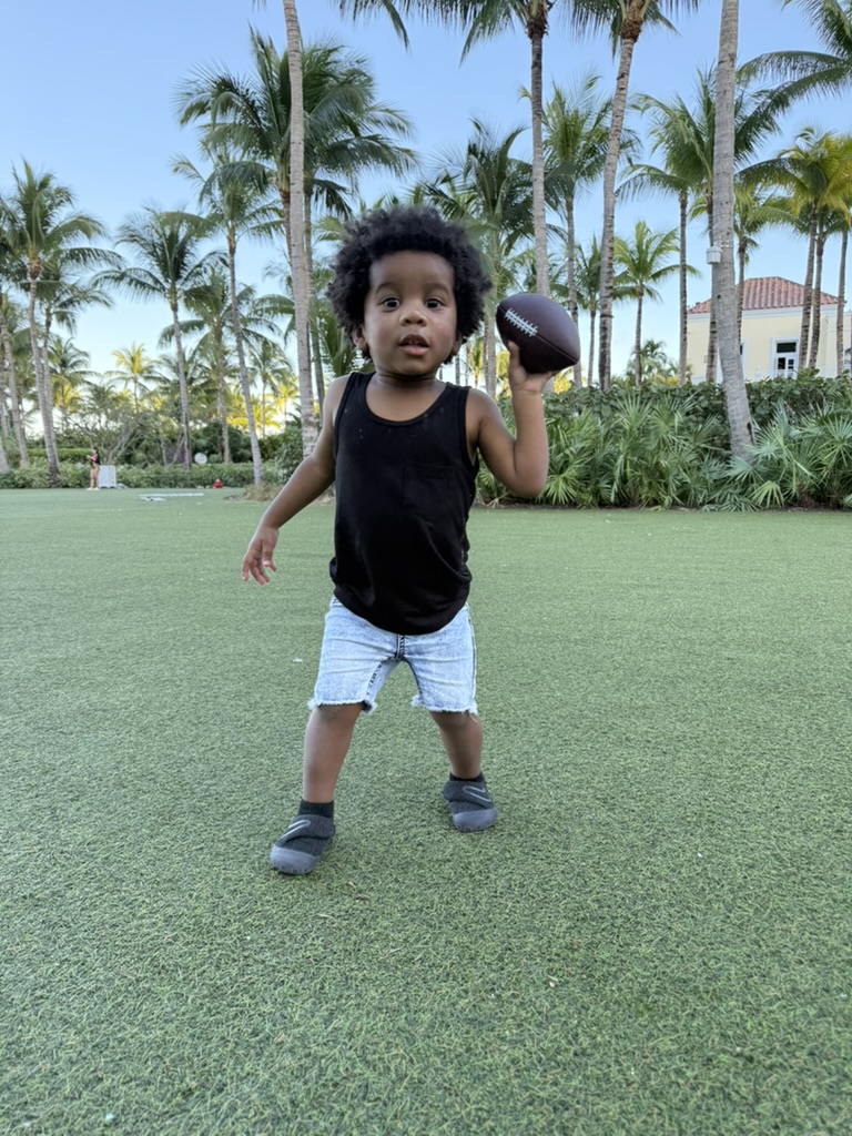 Avery holding a football on the central lawn surrounded by palm trees