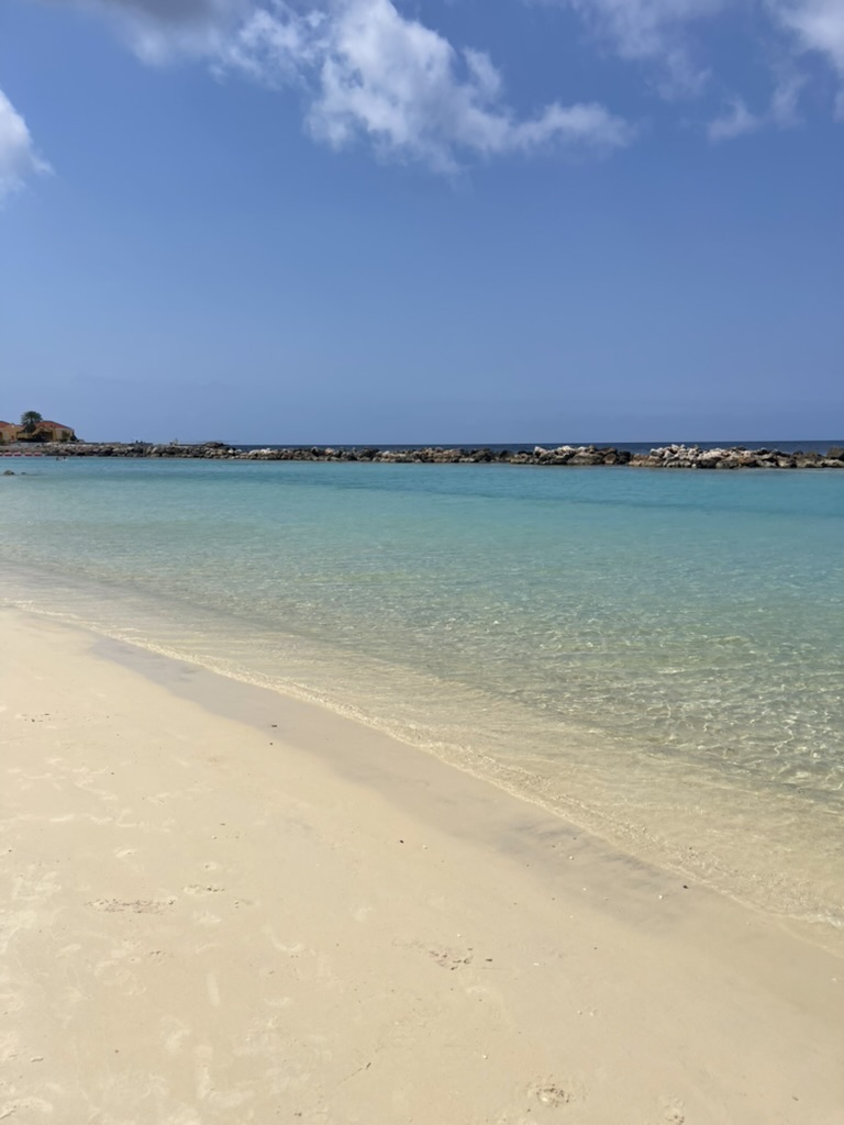 Calm, protected turquoise water and pale sand behind a rock breakwater at Jan Thiel