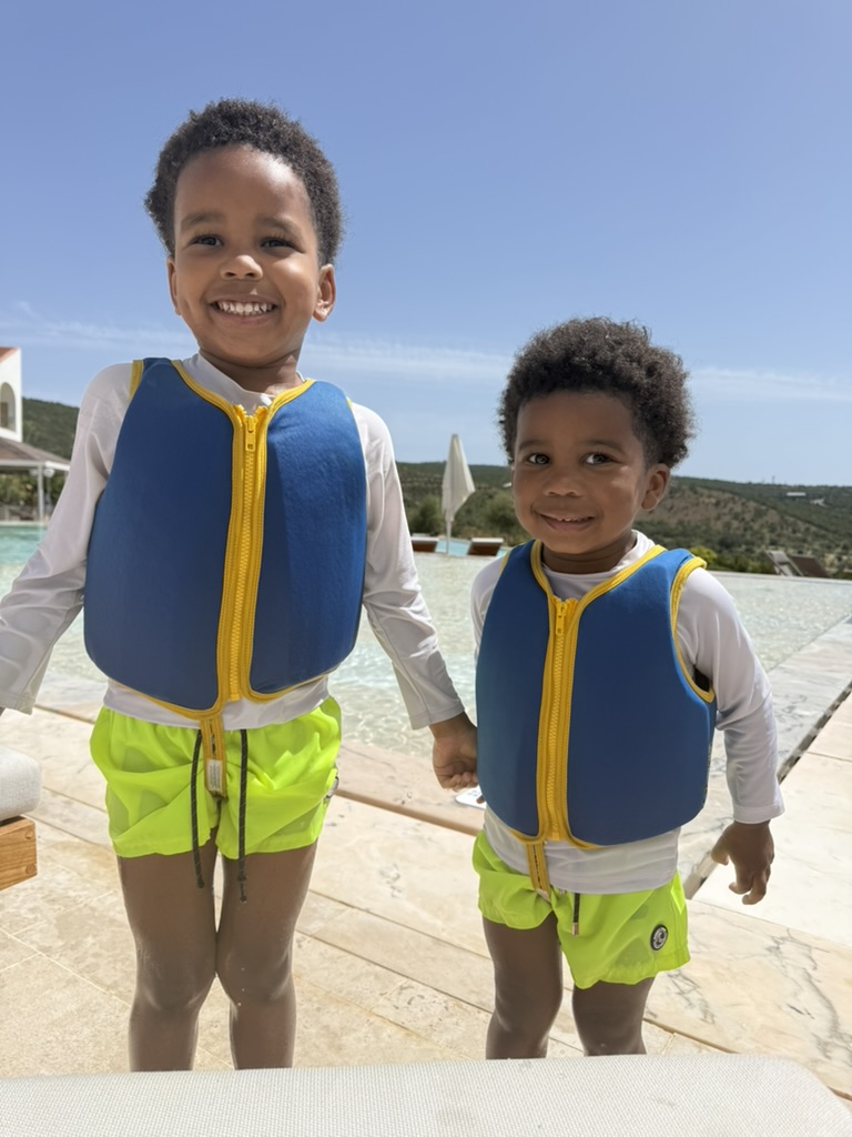 Two boys in blue life jackets standing beside the resort pool with hills behind