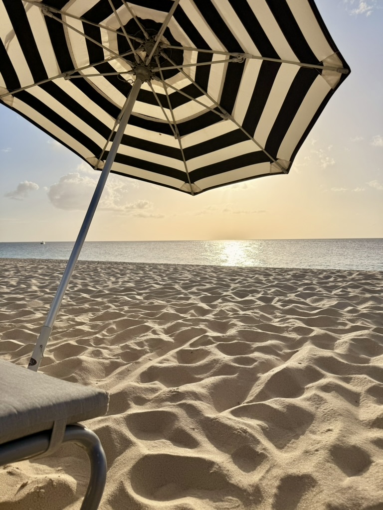 View from a lounger under a black-and-white striped umbrella at sunset