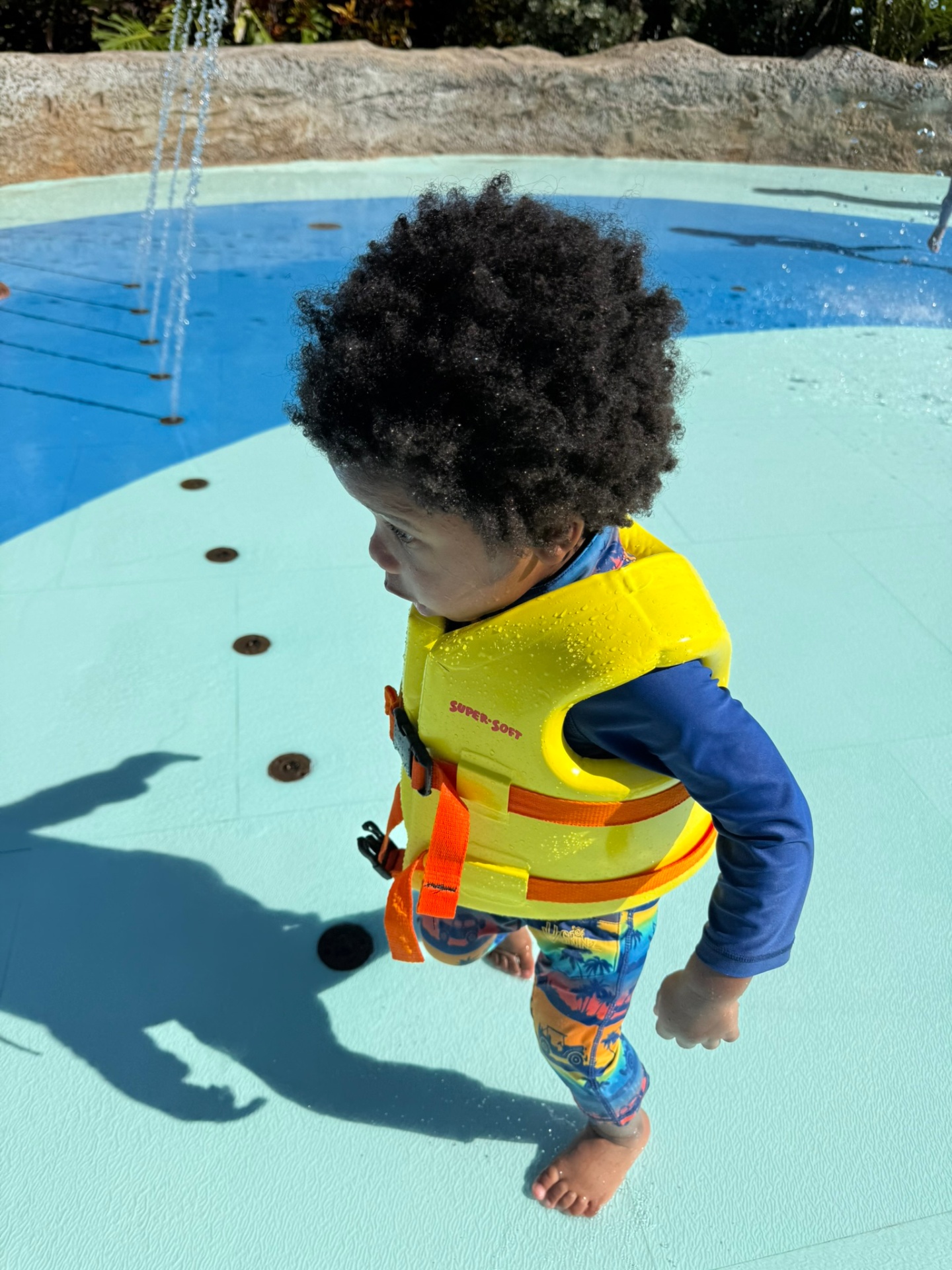 Avery in a life vest walking through the splash pad jets