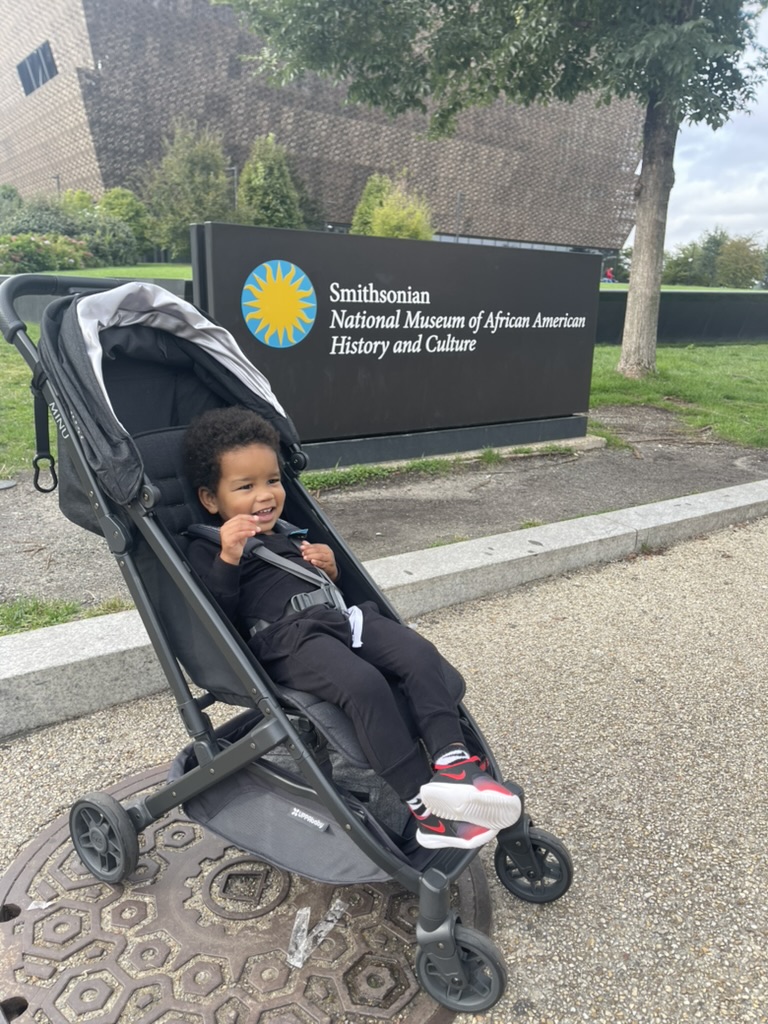 Toddler in a stroller in front of the Smithsonian National Museum of African American History and Culture sign